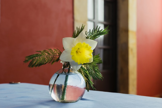  floral arrangement on a White fabric tablecloth. Glass vase centerpiece with a narcissus. Elegant vintage restaurant background