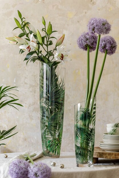 Floral composition at kitchen interior with wooden family table, beautiful flowers in vase, plates, cups, tray and elegant decoration. Dining room in modern home decor. Template.