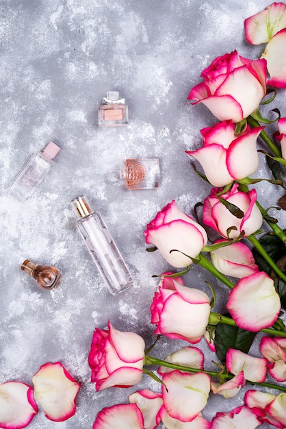 Floral frame composition with roses and many different perfume bottles on stone background. 