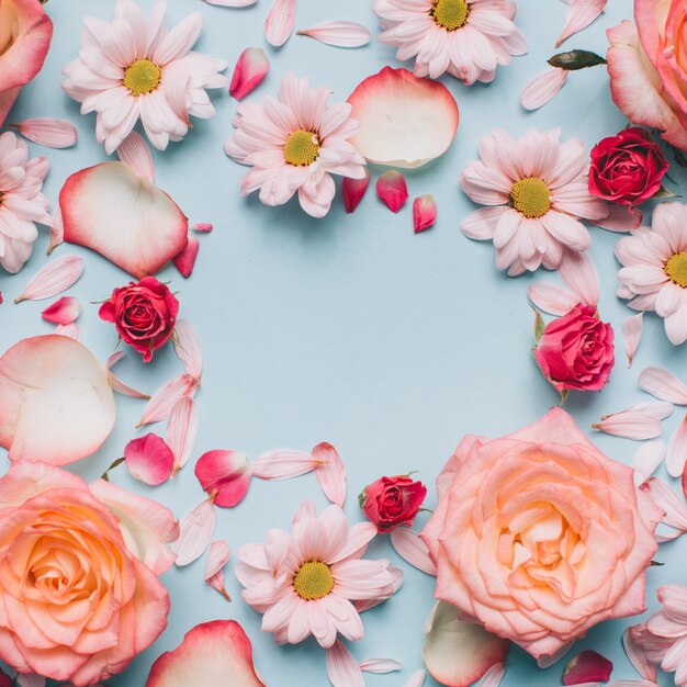 Floral pattern of roses buds, camomiles and petals on blue background. 