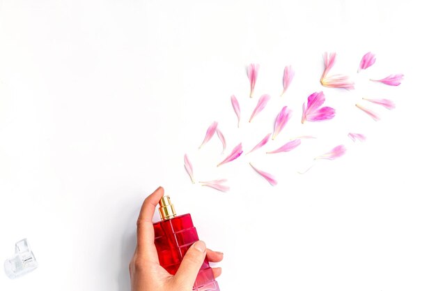 Фото Концепция цветочного аромата бутылка парфюмерии в женской руке на белом фоне с лепестками пиона