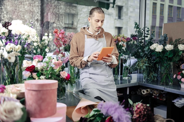 Floral shop. Attentive designer spending pause with gadget while checking news