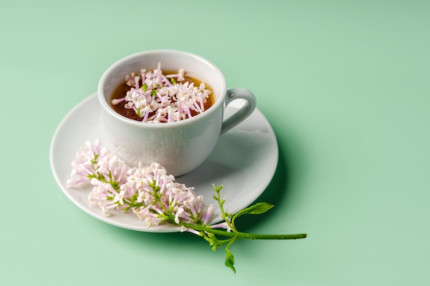 Floral spring composition and a mug of tea on a green background top view copy space