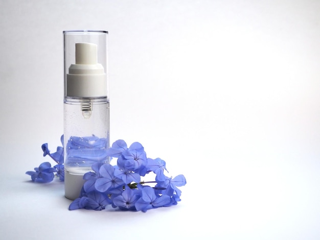 Цветочный гидролат воды в прозрачной бутылке и синие цветы на белом фоне