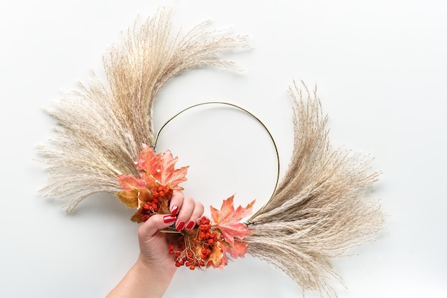 Floral wreath from dry pampas grass and Autumn leaves Hands tie decorations to metal frame