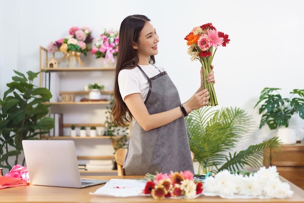 花屋のコンセプト 女性の花屋は、店で花束を作る準備をするためにカラフルなガーベラを保持しています