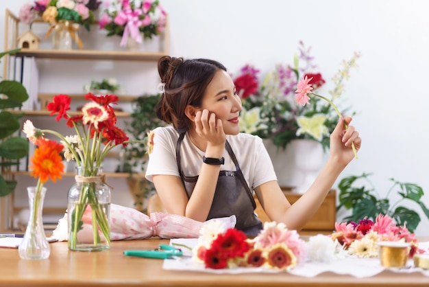 花屋のコンセプト女性の花屋は手にあごに触れ、店でピンクのガーベラを握りながら微笑む