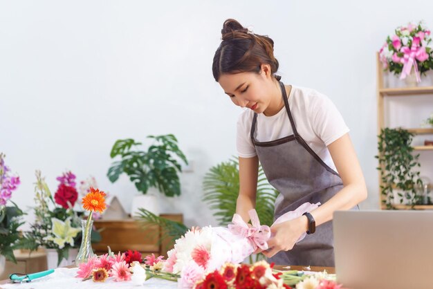 花屋のコンセプト 女性の花屋が紙とリボンの弓でカラフルな花束を包み、作成します