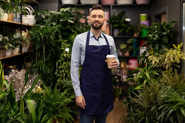 花と鉢植えの植物に囲まれた彼の店で花屋の起業家は一杯のコーヒーで立っています