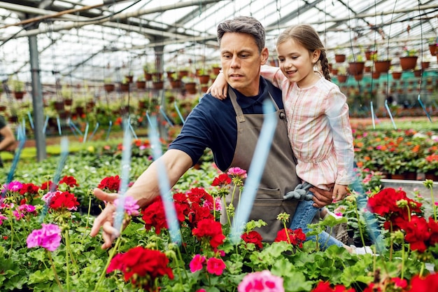 Florist holding his daughter and showing her flowers while working in a greenhouse