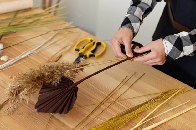 Il fiorista fa un bel mazzo di fiori secchi su un tavolo di legno, primo piano