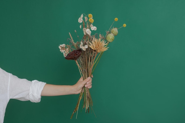 Florist makes a bouquet of dried flowers at a wooden table on a plain dark background with copyspace