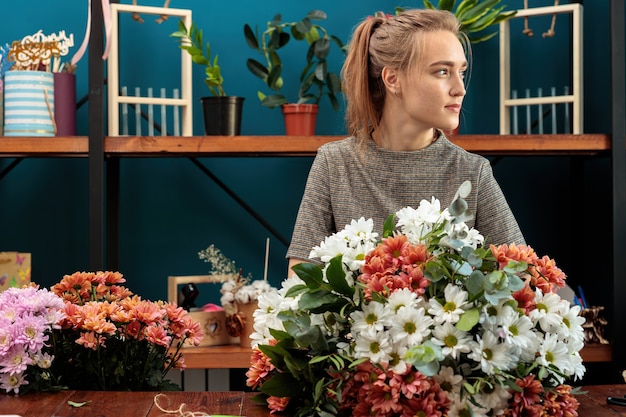 꽃집은 여러 가지 빛깔의 국화 꽃다발을 만듭니다. 한 젊은 성인 소녀가 옆을 바라보고 있습니다.