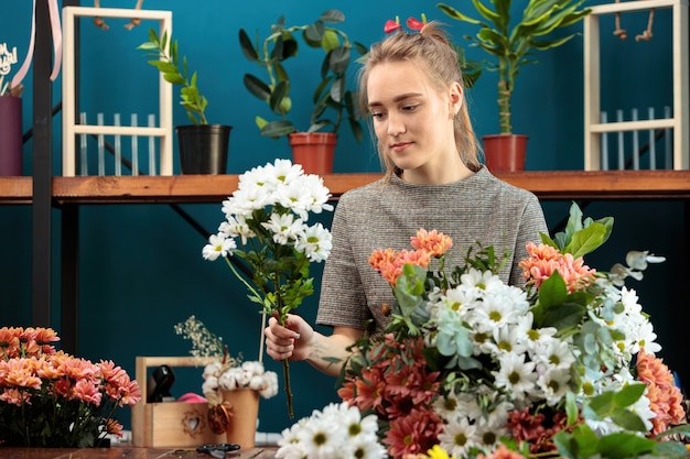 Photo florist makes a bouquet of multi-colored chrysanthemums. a young adult girl works with enthusiasm.