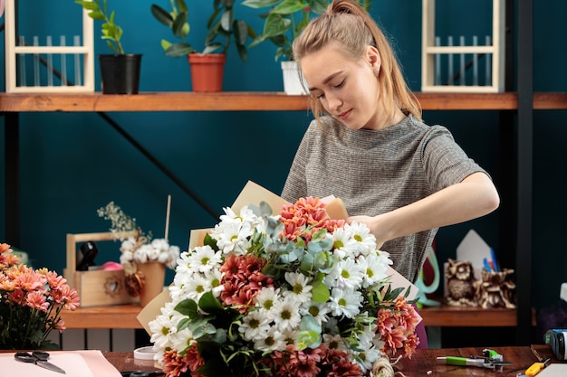 Florist makes a bouquet of multi-colored chrysanthemums. A young adult girl works with enthusiasm.