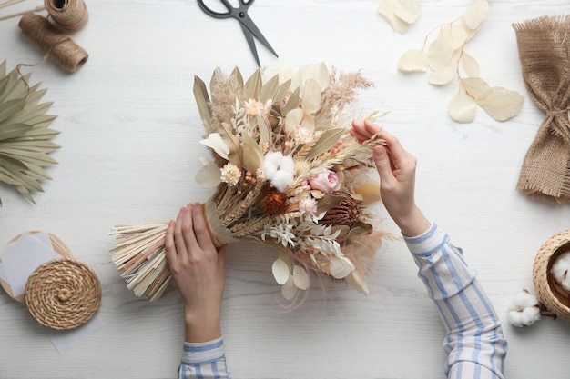 Florist making beautiful bouquet of dried flowers at white table top view