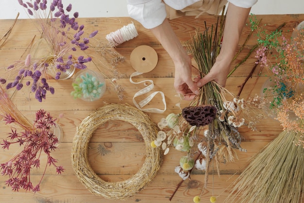 Florist making bouquet of dried flowers at wooden table top view Materials for making herbarium