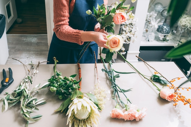 사진 florist의 창의적인 작업에는 스타일의 아름다움과 비율이 필요합니다. 장미, 달리아, 카네이션에서 아름다운 꽃꽂이를 만드는 여자