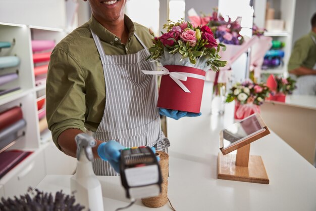 Florist shop manager giving a card-scanning machine to a client while holding a ribbon-wrapped pot in his hand