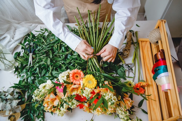 A florist ties a bouquet of fresh flowers with twine on his desk littered with cut leaves