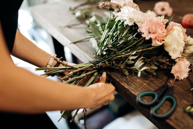 Photo florist ties a ribbon on the stems of flowers in flower shop .