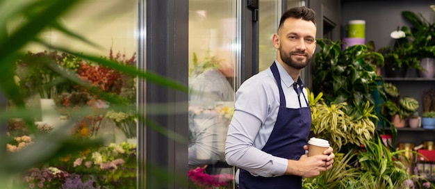 florist with a glass of coffee in aprons on the background of a refrigerator with flowers.