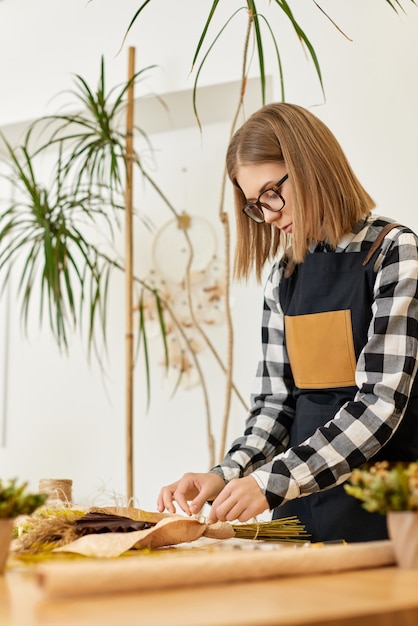 Florist woman makes beautiful bouquet of dried flowers on wooden table