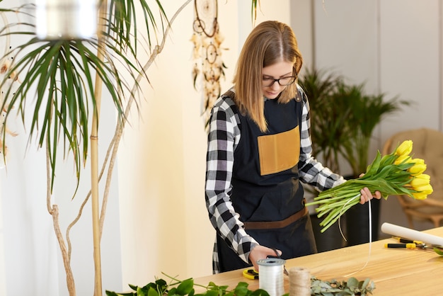 Florist woman makes a bouquet of fresh yellow tulips. Floral design studio