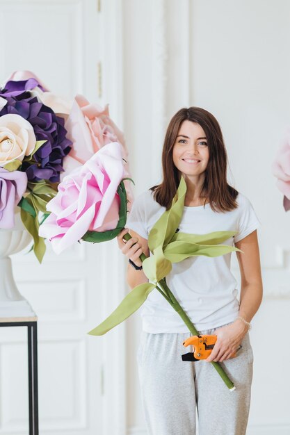 職場の花屋：美しい女性が花束を作り、花屋で働き、装飾を整え、屋内でカジュアルな服装のポーズをとります。縦撮り。女性はバラの束を収集します。中小企業のコンセプト