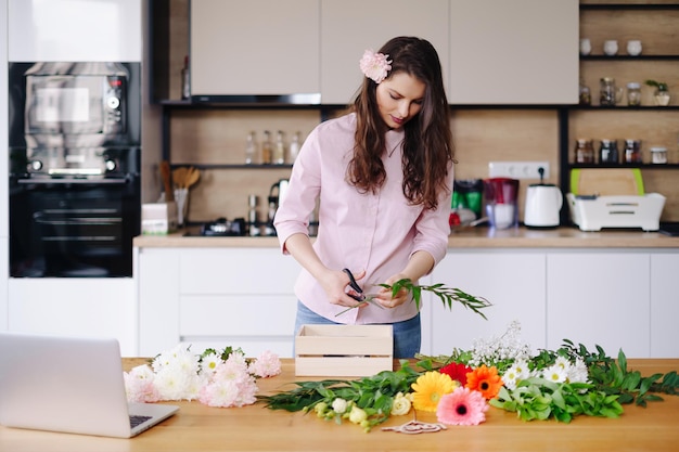 Florist at work pretty young brunette woman making fashion modern composition of different flowers at home