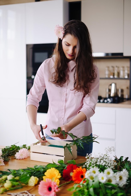 Florist at work pretty young brunette woman making fashion modern composition of different flowers at home