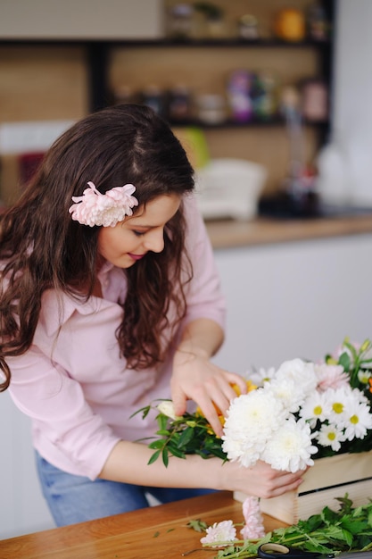 Florist at work pretty young brunette woman making fashion modern composition of different flowers at home