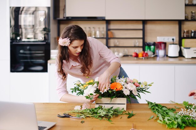 Florist at work pretty young brunette woman making fashion modern composition of different flowers at home