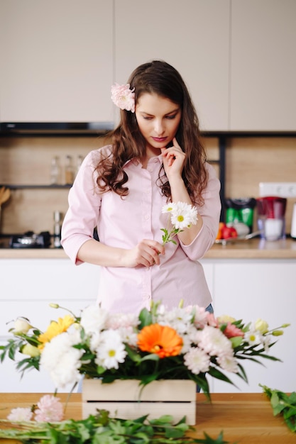 Florist at work pretty young brunette woman making fashion modern composition of different flowers at home