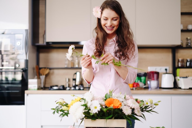 仕事で花屋かなり若いブルネットの女性が自宅でさまざまな花のファッションモダンな構成を作っています