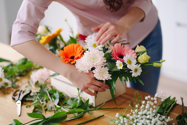 Florist at work young brunette woman hands making fashion modern composition of different flowers at home