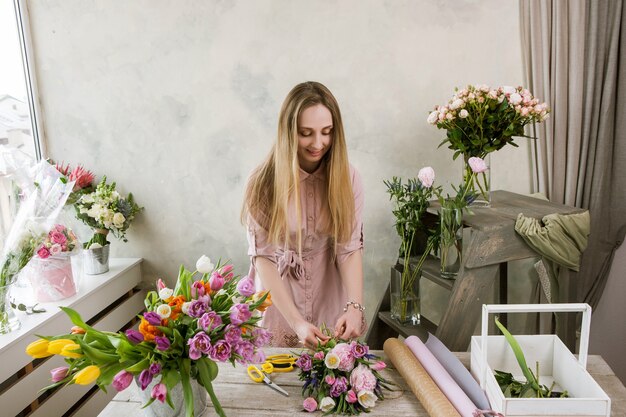 ワークショップの花屋は花束を詰めます。デコレータは彼女の作品で動作します。フローリストリーを組み立てるフラワーショップの女性