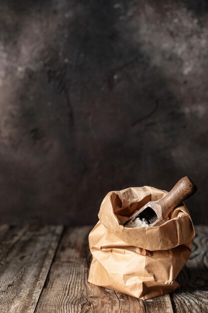 Flour in brown craft paper bag on dark wooden background rustic style copy space