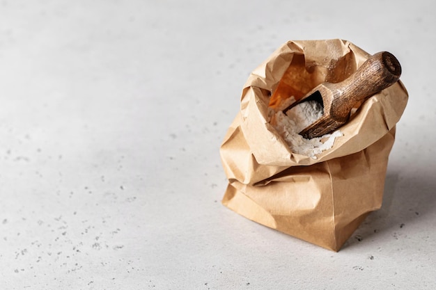 Flour in brown craft paper bag with wooden spoon on white background rustic style copy space