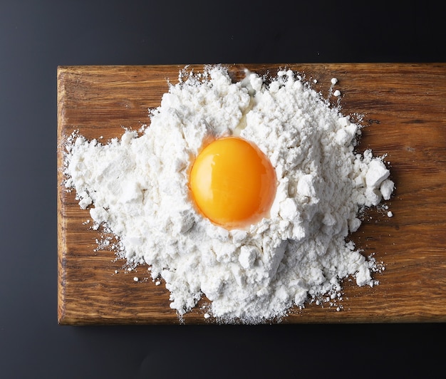 Flour and egg yolk on wooden cutting board, top view