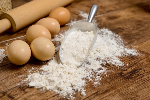 Flour, eggs and rolling pin on wooden table.