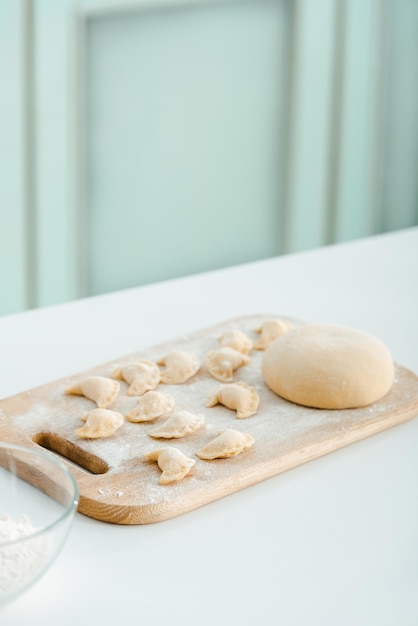 Flour near raw dumplings on wooden cutting board