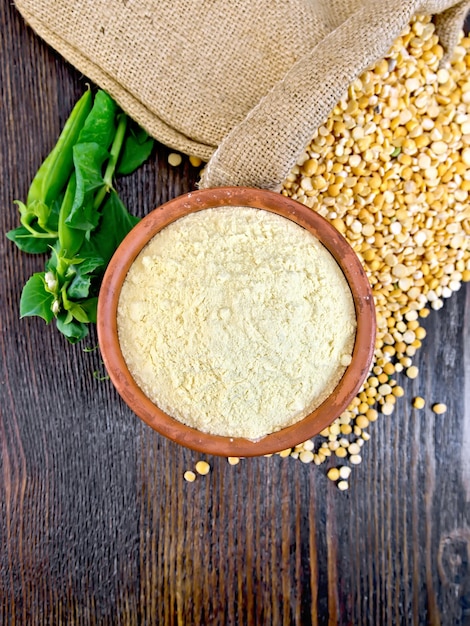 Flour pea in a clay bowl flakes in a bag and fresh pods on a background of wooden boards on top