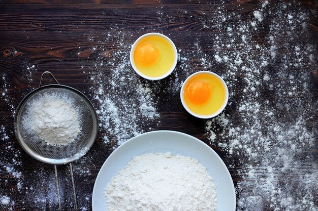 Photo flour powder sprinkled on wood table, eggs, sieve, table filled with flour.