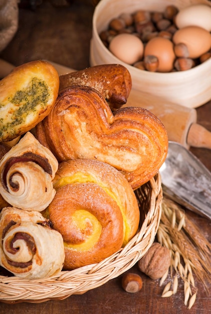 Flour products of various types Wicker basket with different types of bread and sweet buns on a wooden table