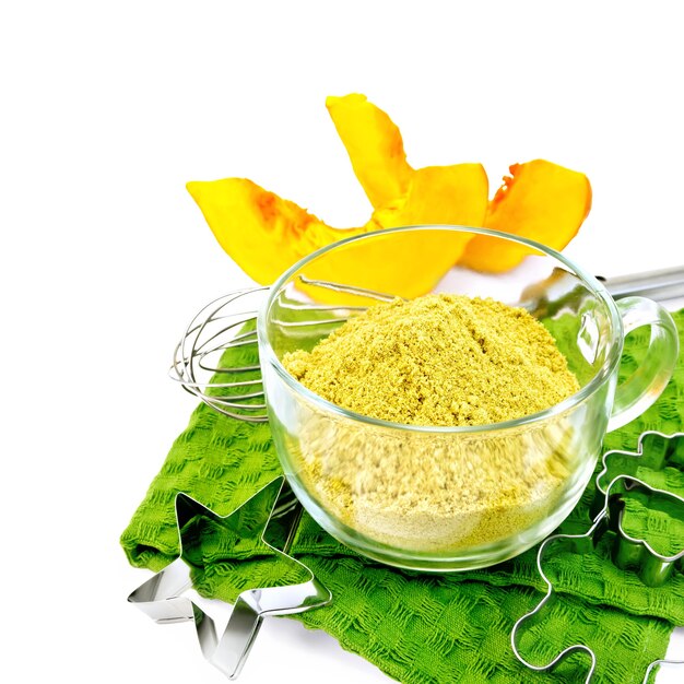 Flour pumpkin in a glass cup, mixer, cookie cutters on a green towel, two slices of vegetables isolated on white background