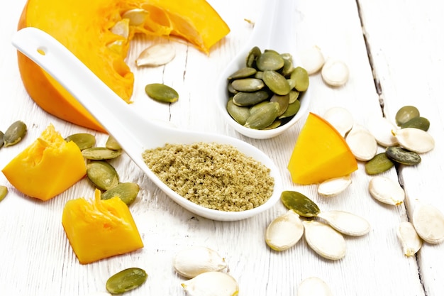 Flour and pumpkin seeds in spoons, slices of vegetable on a background of a light wooden board