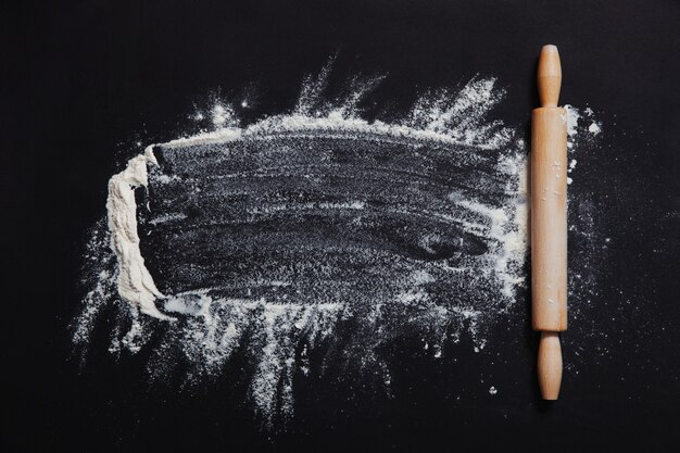 Flour and rolling pin on the black background