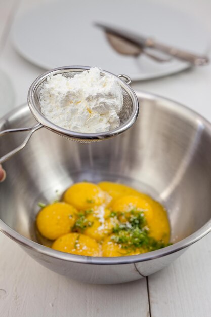 Flour in strainer over egg yolk in bowl at table