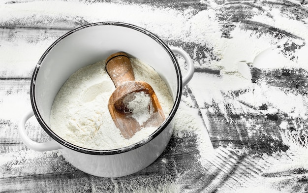 Photo flour with a shovel in a saucepan. on the stone table.